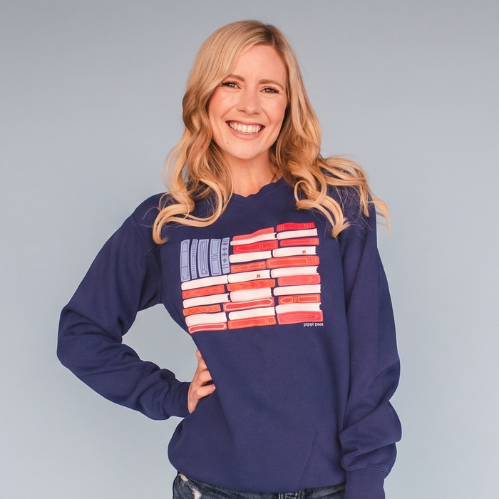 Woman wearing a navy blue sweatshirt with a colorful illustration of an American flag made out of books.