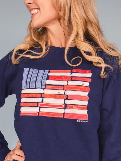 Close-up of a woman wearing a navy blue sweatshirt with a colorful illustration of an American flag made out of books.