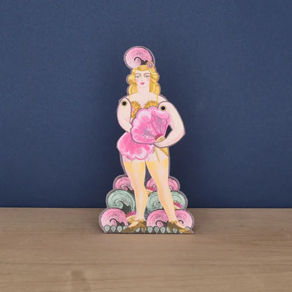A freestanding die-cut card featuring a vintage-style illustration of a blonde fan dancer in a showgirl outfit, holding a large pink feather fan.