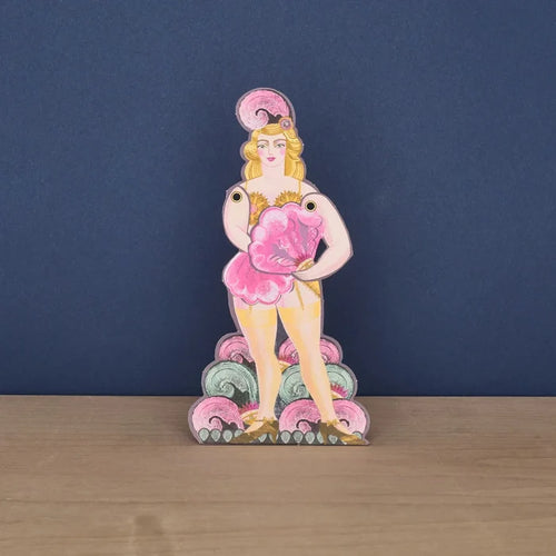 A freestanding die-cut card featuring a vintage-style illustration of a blonde fan dancer in a showgirl outfit, holding a large pink feather fan.