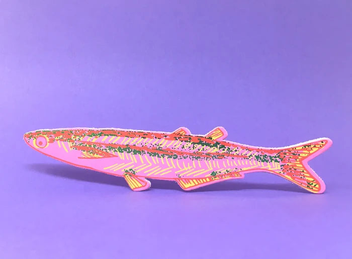 A fish-shaped bookmark with a pink base, yellow striped pattern, and multicolored glitter details, displayed against a solid purple background.