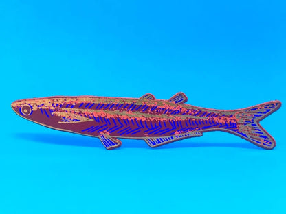 A fish-shaped bookmark with a dark red base, royal blue striped pattern, and multicolored glitter details, displayed against a solid blue background.