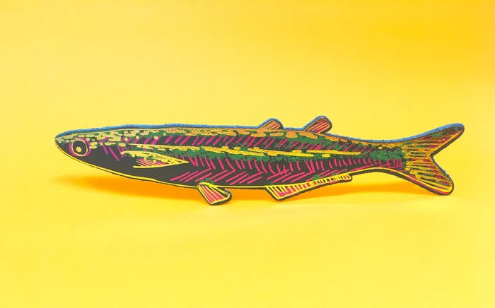 A fish-shaped bookmark with a dark green base, hot pink striped pattern, and multicolored glitter details, displayed against a solid yellow background.