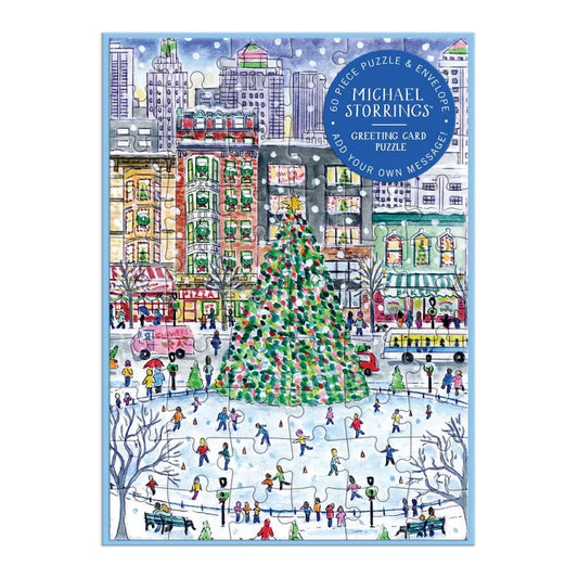 A square jigsaw puzzle notecard cover featuring a colorful winter city scene with a large decorated Christmas tree, skaters in an ice rink, buildings, and people. A blue circular badge at the top right reads 'Michael Storring's Greeting Card Puzzle'.