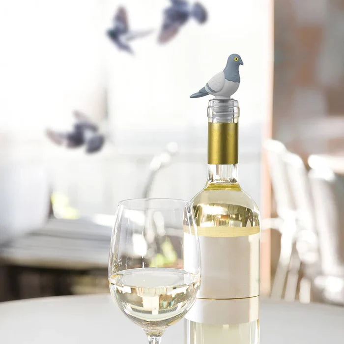 Wine bottle with a pigeon-shaped bottle stopper next to a glass of white wine on a blurred background.