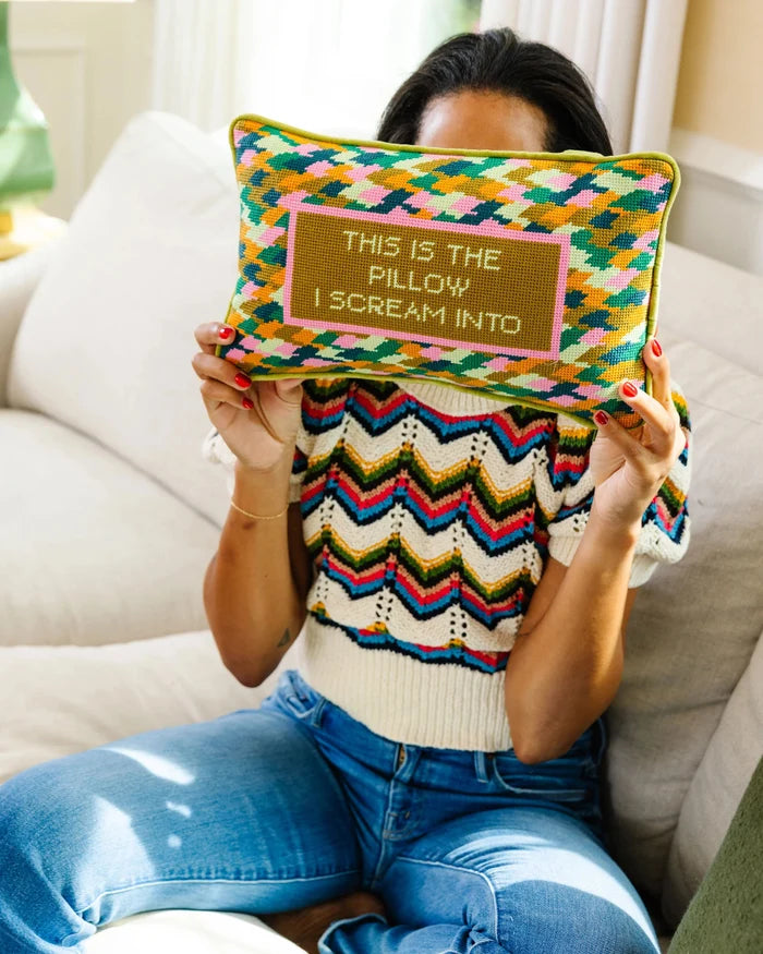 Person holding a colorful pillow with text, sitting on a couch.