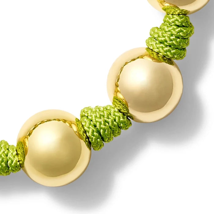 Bracelet with gold and textured apple green threads on a white background