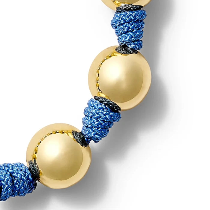 Bracelet with gold beads and blue cord on a white background