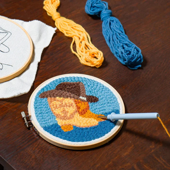 Embroidery hoop with a completed design of a pair of boots wearing a hat on a wooden surface.